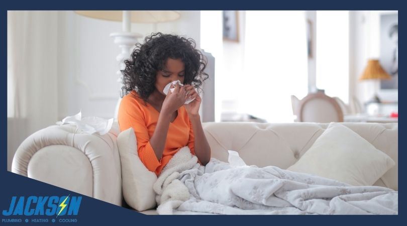 Woman lays on couch while blowing her nose into tissues
