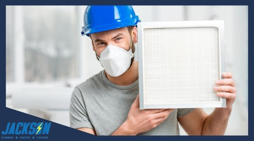 HVAC technician wearing mask and helmet holds up HEPA filter
