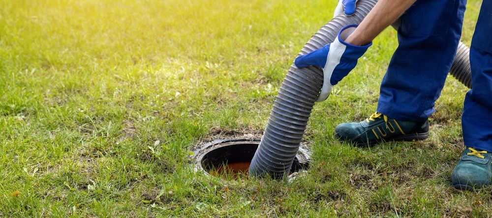 Septic plumber holding septic pumping pipe being used to empty septic tank in yard